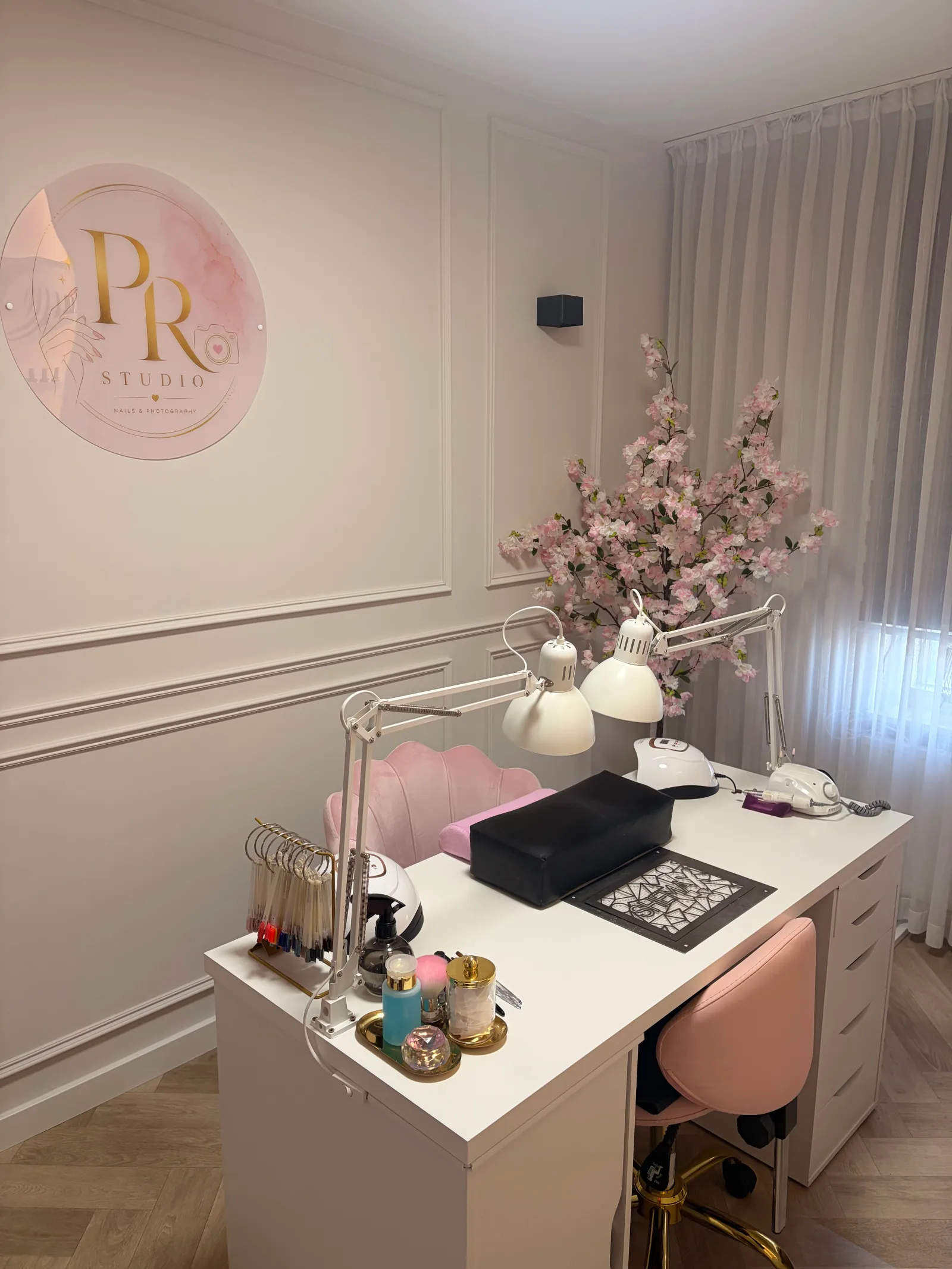 De manicuretafel van PR Studio met het logo aan de wand, werklampen en een bloesemtak