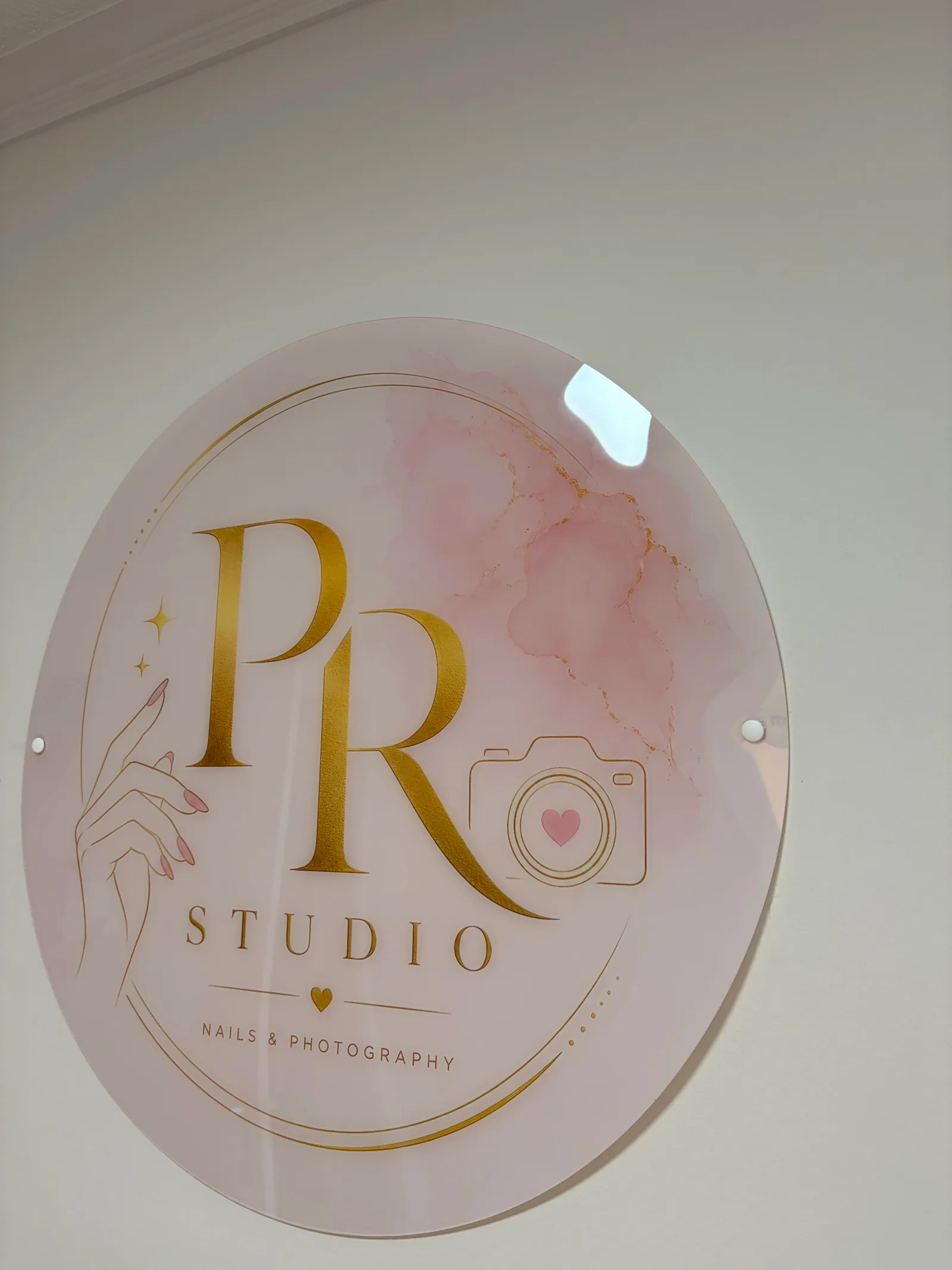 Het logobord van PR Studio in roze acryl met gouden opdruk, aan de wand van de studio